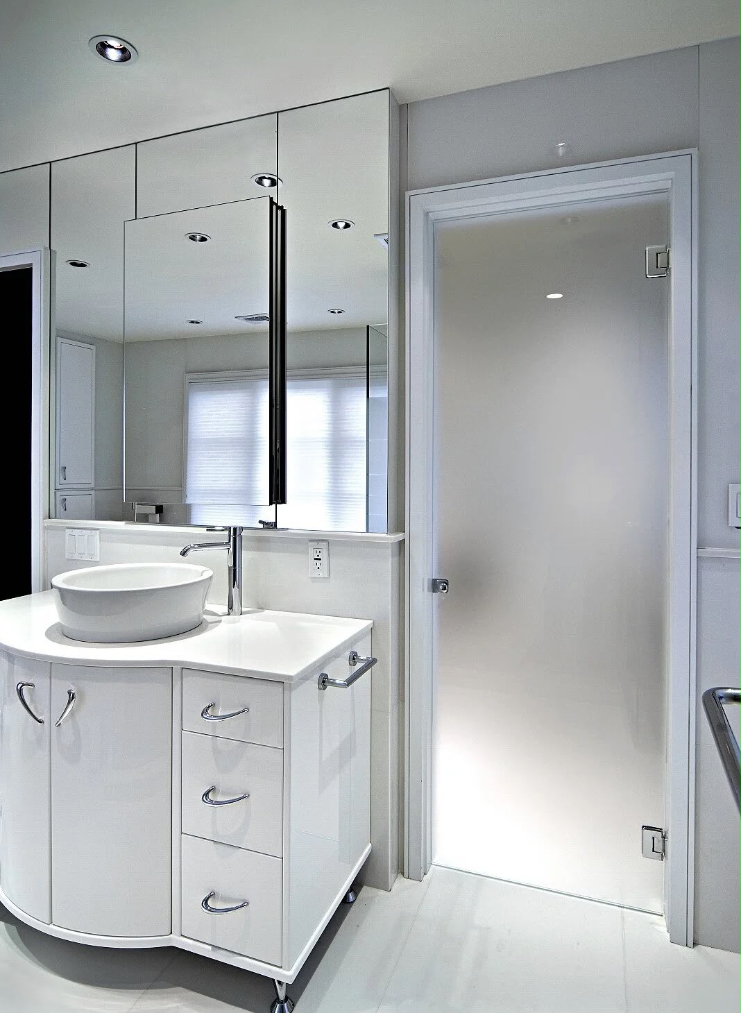 White minimalist bathroom with curved vanity and frosted glass door